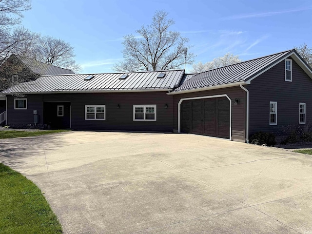 ranch-style house with a standing seam roof, concrete driveway, metal roof, and a garage