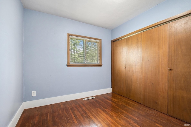 unfurnished bedroom with baseboards, visible vents, wood finished floors, and a closet