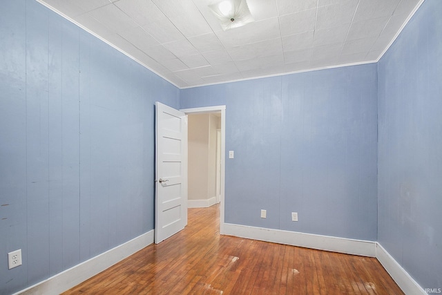 unfurnished room with crown molding, wood walls, baseboards, and hardwood / wood-style flooring