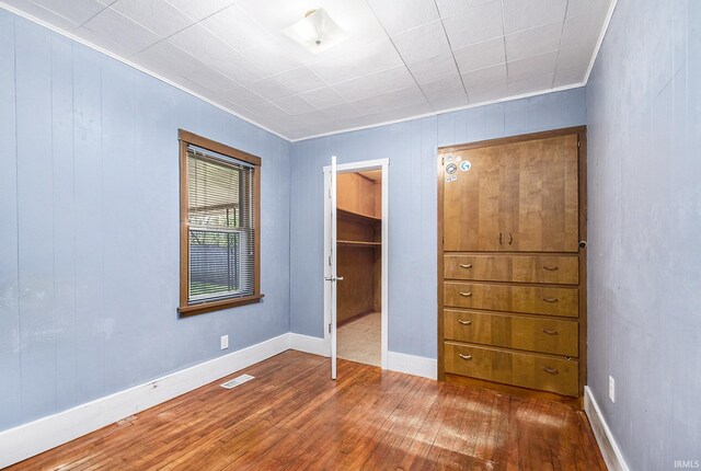 unfurnished bedroom with visible vents, crown molding, a closet, wood finished floors, and a walk in closet