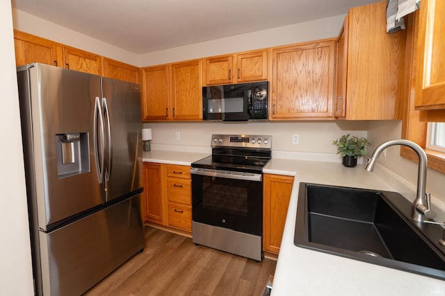 kitchen with wood finished floors, light countertops, brown cabinets, a sink, and appliances with stainless steel finishes