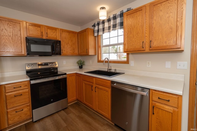 kitchen featuring brown cabinetry, dark wood-style flooring, a sink, light countertops, and stainless steel appliances