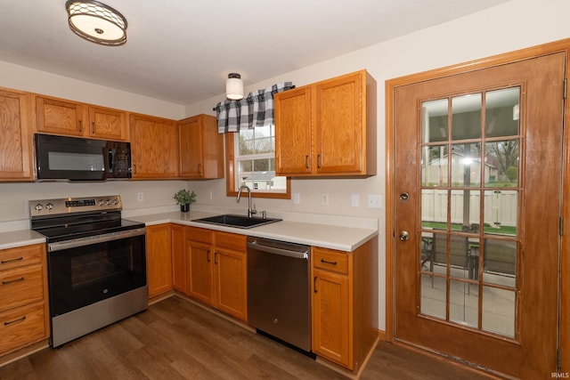 kitchen with brown cabinets, dark wood-style flooring, a sink, light countertops, and stainless steel appliances