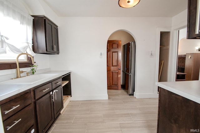 kitchen featuring a sink, arched walkways, dark brown cabinetry, and light countertops