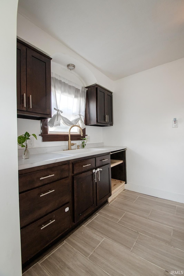 kitchen featuring baseboards, a sink, dark brown cabinets, and light countertops