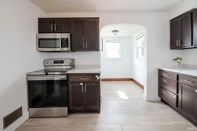 kitchen with dark brown cabinetry, visible vents, appliances with stainless steel finishes, arched walkways, and light countertops