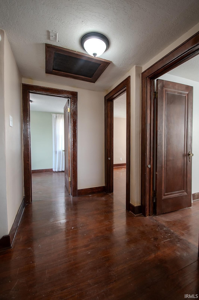 hallway with baseboards, a textured ceiling, and dark wood-type flooring