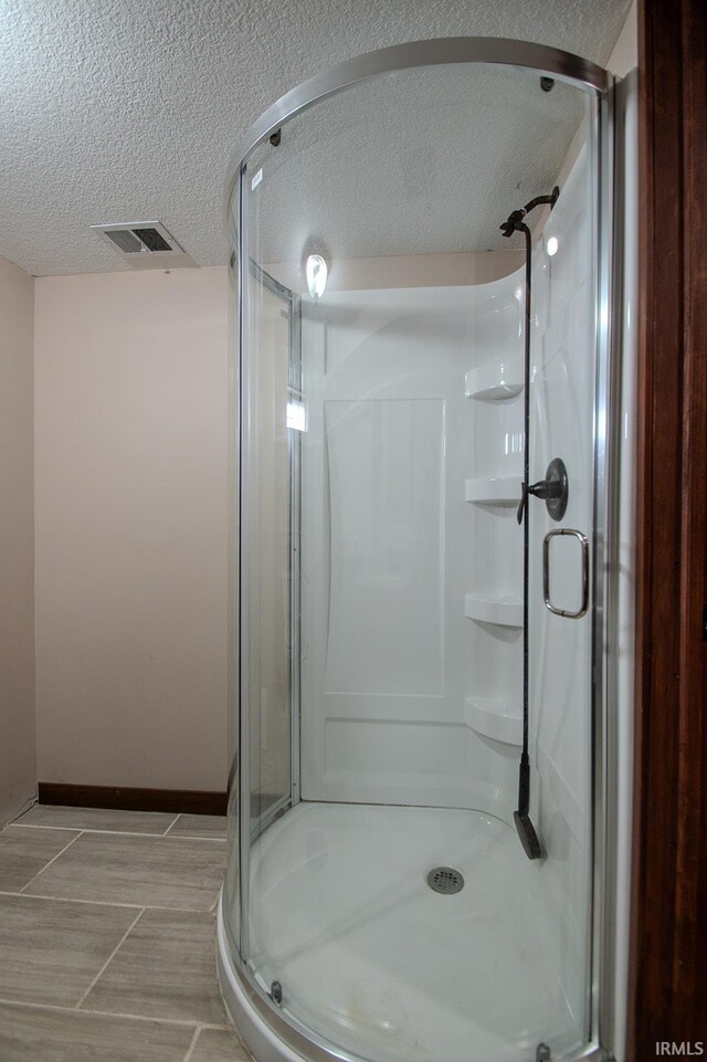 bathroom featuring a textured ceiling, visible vents, a shower stall, and baseboards