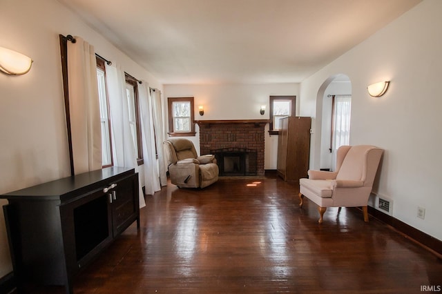 living area featuring a healthy amount of sunlight, a brick fireplace, dark wood-style floors, and visible vents