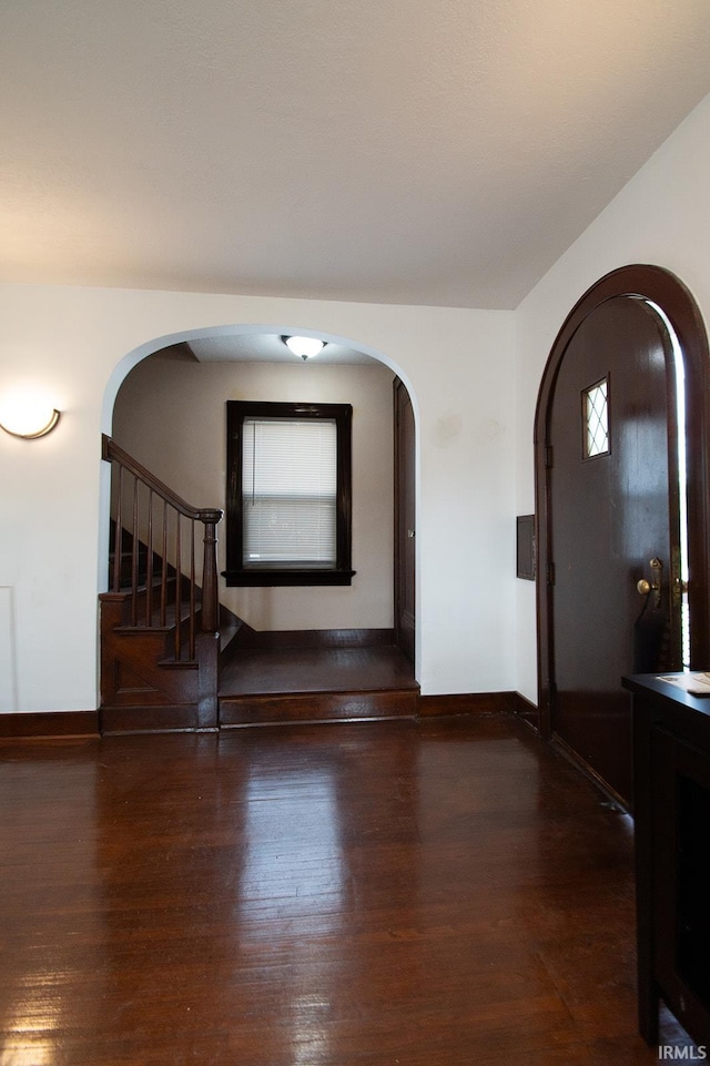 foyer featuring baseboards, arched walkways, stairs, and wood finished floors
