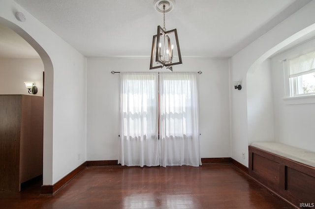unfurnished dining area featuring baseboards, arched walkways, dark wood-style flooring, and an inviting chandelier