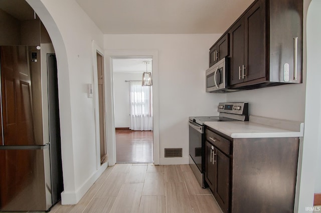 kitchen with arched walkways, dark brown cabinetry, appliances with stainless steel finishes, and visible vents