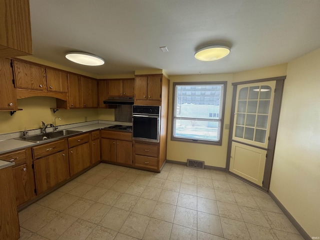 kitchen with oven, brown cabinetry, and a sink