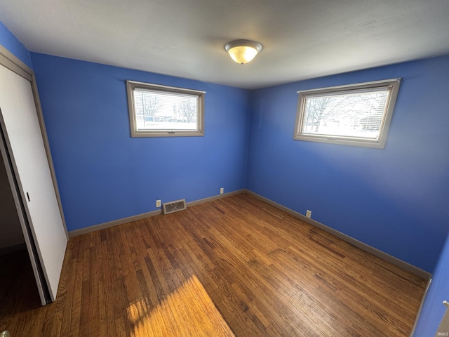 unfurnished bedroom featuring baseboards, a closet, wood finished floors, and visible vents
