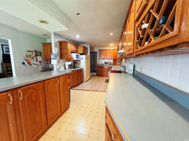 kitchen with brown cabinetry, white appliances, recessed lighting, a textured ceiling, and under cabinet range hood
