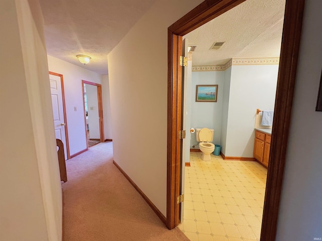 hallway featuring a textured ceiling, visible vents, and baseboards