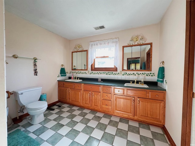 bathroom with double vanity, toilet, visible vents, and a sink