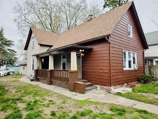 view of front facade featuring a porch, a chimney, and roof with shingles