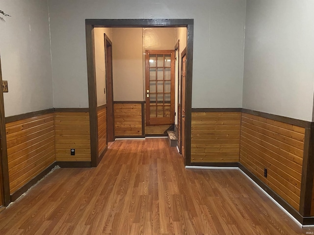 empty room featuring wooden walls, wainscoting, and wood finished floors