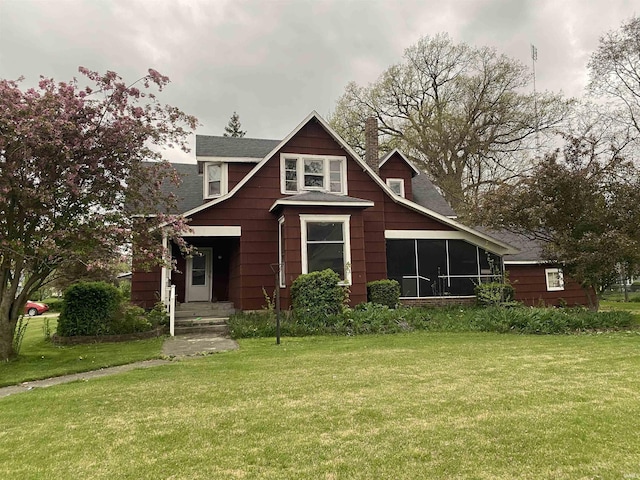 view of front of property with a chimney, a shingled roof, a sunroom, and a front lawn