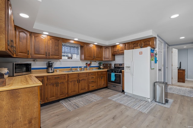 kitchen featuring brown cabinets, appliances with stainless steel finishes, a sink, light wood-style floors, and light countertops