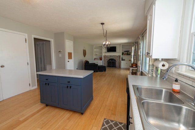 kitchen with a sink, a fireplace, light wood-style flooring, open floor plan, and blue cabinets