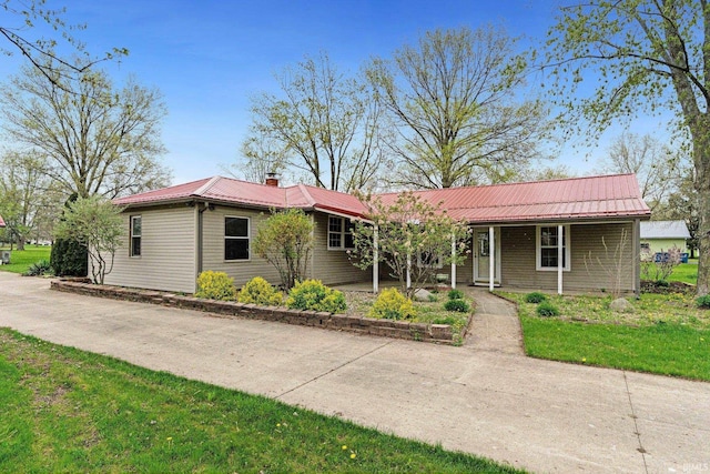 ranch-style house featuring a porch, a chimney, and metal roof