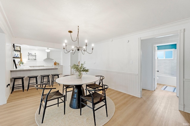 dining area with light wood-style floors, crown molding, a wainscoted wall, and an inviting chandelier