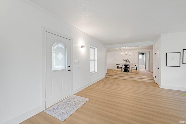 entryway with an inviting chandelier, baseboards, ornamental molding, and light wood-style flooring