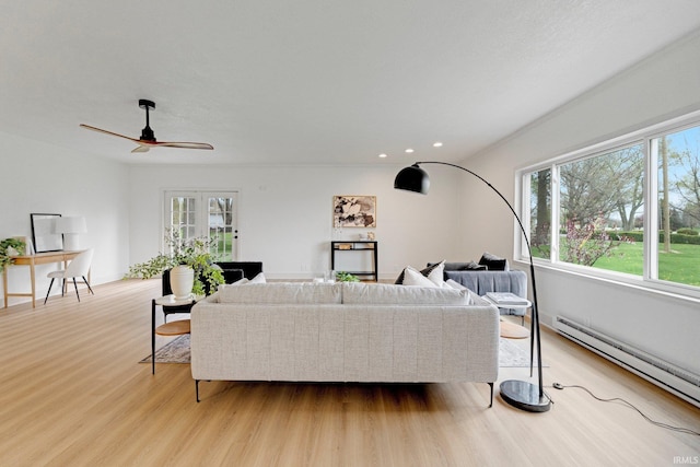 living area with ceiling fan, a wealth of natural light, baseboard heating, and light wood finished floors