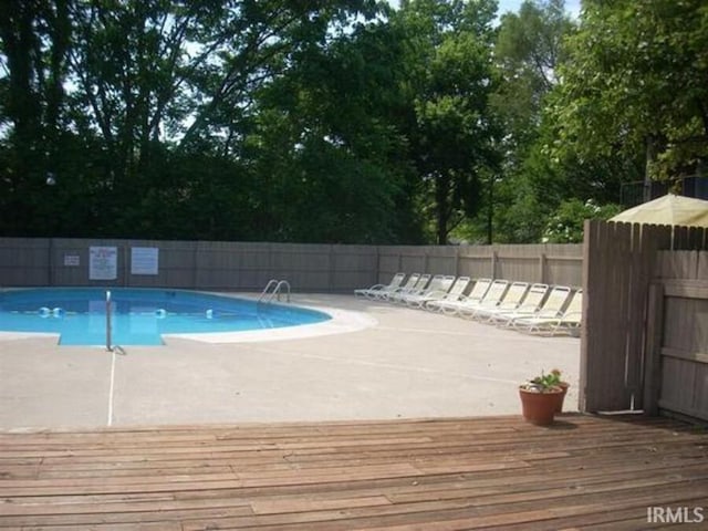 pool with a patio area, fence, and a deck