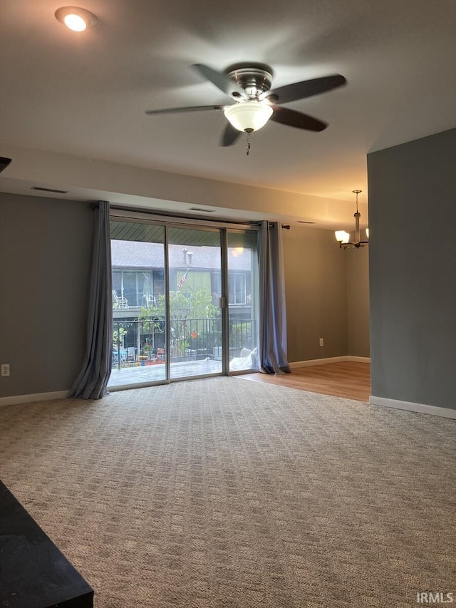 empty room featuring carpet floors, baseboards, and ceiling fan with notable chandelier