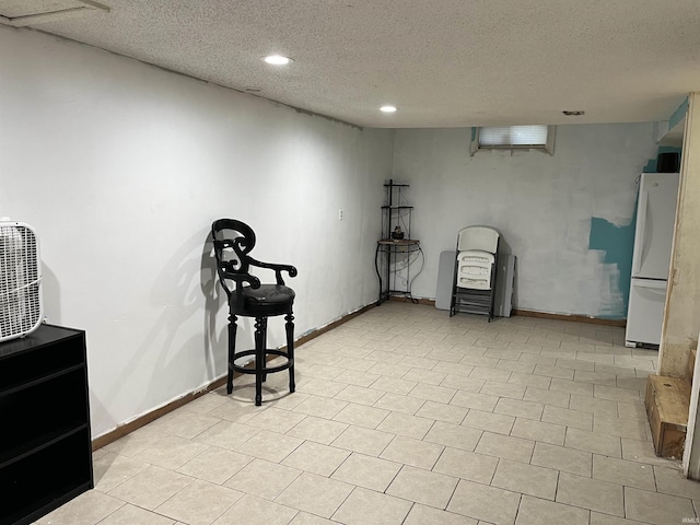 finished below grade area featuring freestanding refrigerator, recessed lighting, a textured ceiling, and baseboards