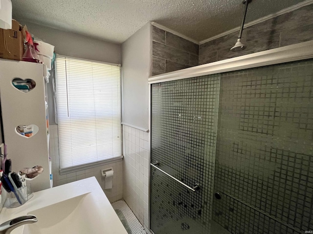 full bathroom with a textured ceiling, tile walls, a shower stall, and a wainscoted wall