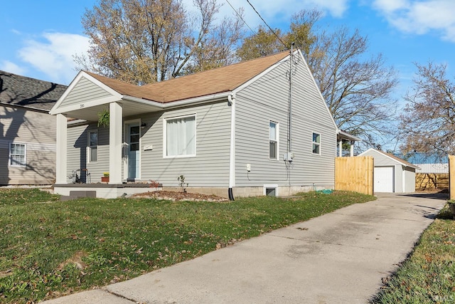 bungalow-style house featuring covered porch, roof with shingles, a front yard, an outbuilding, and a detached garage