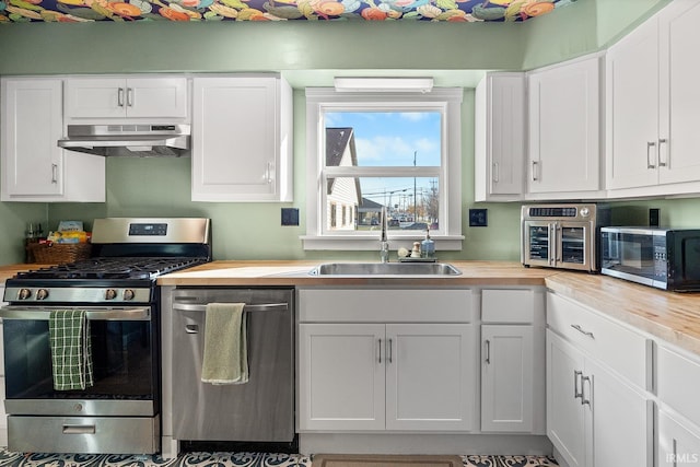 kitchen with under cabinet range hood, white cabinetry, butcher block countertops, and appliances with stainless steel finishes