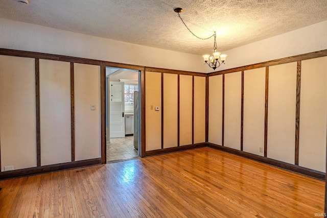 empty room featuring an inviting chandelier, a textured ceiling, and light wood-style flooring