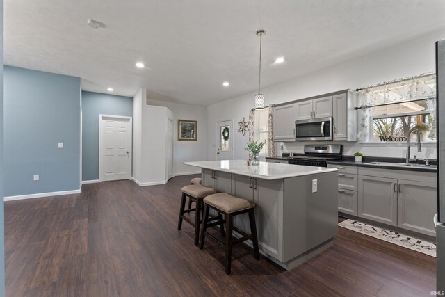 kitchen with dark wood-type flooring, a center island, a sink, appliances with stainless steel finishes, and gray cabinetry