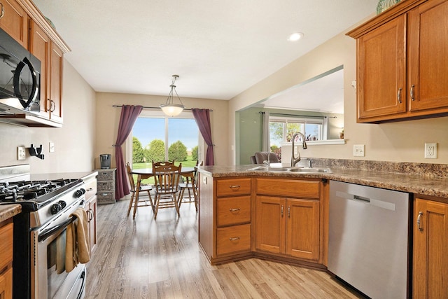 kitchen with brown cabinets, stainless steel appliances, a sink, and light wood-style floors