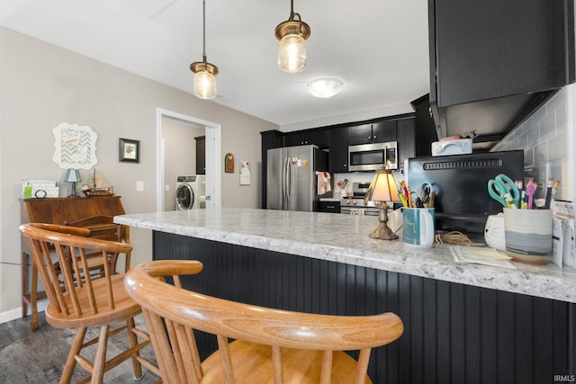 kitchen featuring a kitchen breakfast bar, a peninsula, dark wood-style floors, dark cabinetry, and stainless steel appliances