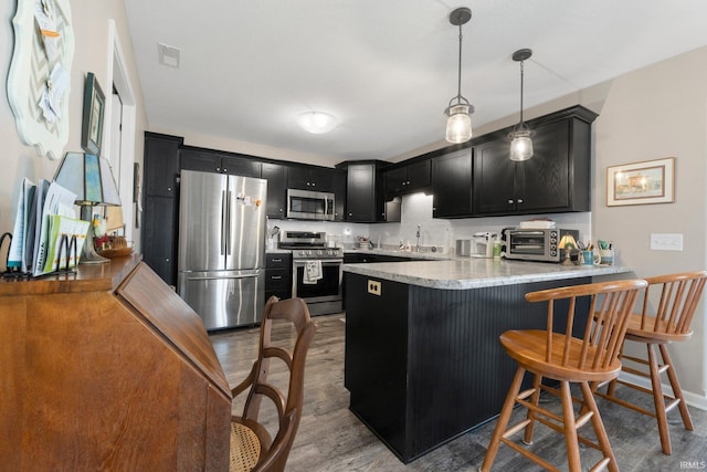 kitchen featuring a peninsula, wood finished floors, light countertops, dark cabinets, and stainless steel appliances