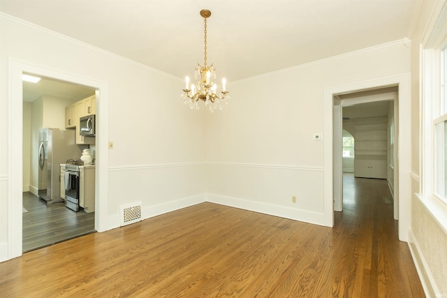 unfurnished dining area with an inviting chandelier, ornamental molding, wood finished floors, and visible vents