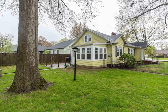 back of house featuring a lawn, a shingled roof, fence, and a chimney