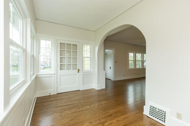 unfurnished room with arched walkways, baseboards, wood finished floors, and visible vents