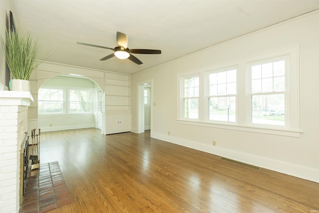 unfurnished living room featuring ceiling fan, visible vents, a brick fireplace, wood finished floors, and baseboards