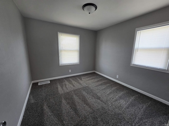 unfurnished room featuring baseboards, dark colored carpet, and visible vents
