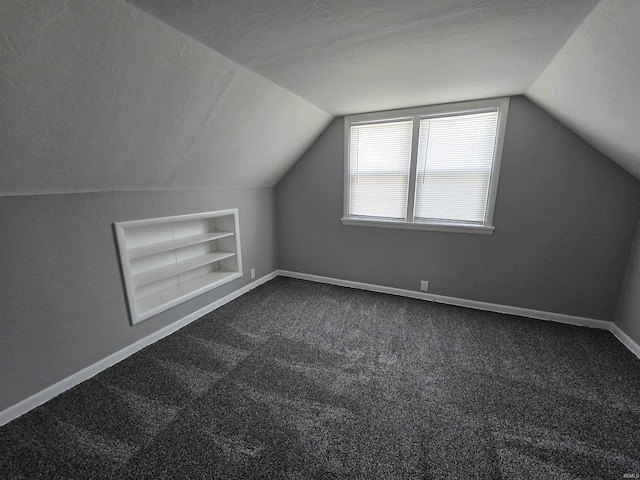 additional living space with baseboards, vaulted ceiling, dark carpet, and built in shelves