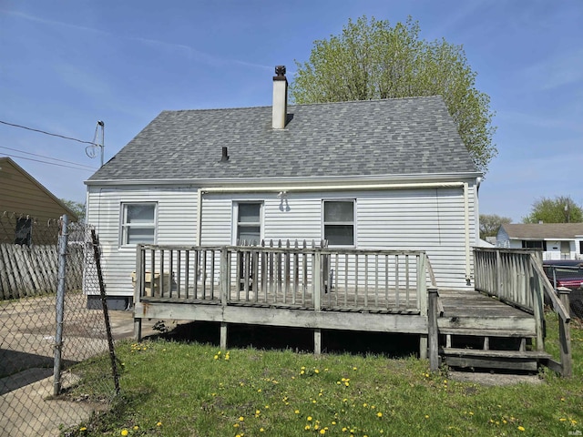 back of house with fence, a shingled roof, a deck, a chimney, and a lawn