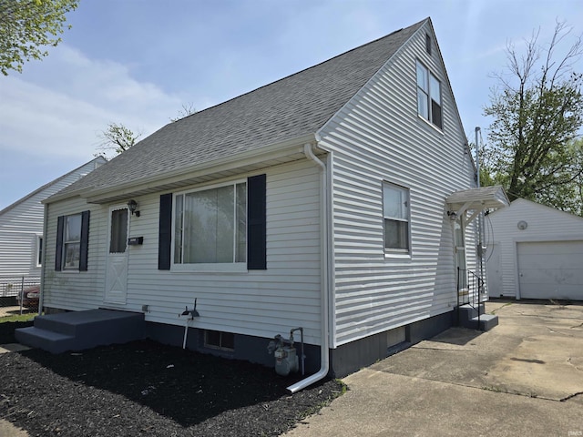 view of side of home with an outdoor structure, roof with shingles, driveway, and a detached garage