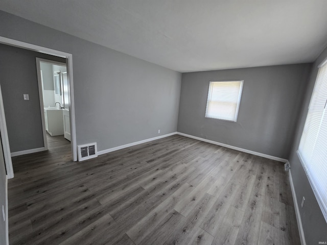 empty room with a sink, baseboards, wood finished floors, and visible vents